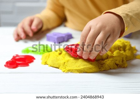 Little child playing with yellow kinetic sand at white wooden table, closeup
