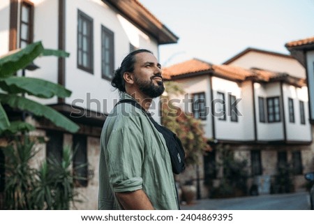 Portrait of a male tourist on a picturesque street of the old town.  A young, handsome guy in a light shirt walks through the green, narrow streets of the ancient city center Royalty-Free Stock Photo #2404869395