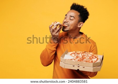 Young happy man he wears orange sweatshirt casual clothes holding italian pizza in cardboard flatbox isolated on plain yellow background. Proper nutrition healthy fast food unhealthy choice concept