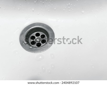 clean white porcelain sink with a shiny stainless steel drain surrounded by sparkling water droplets. It is perfect for showcasing plumbing services, home hygiene articles Royalty-Free Stock Photo #2404892107