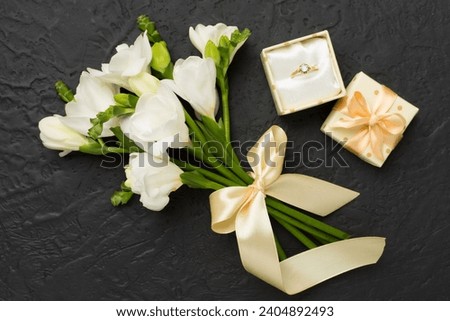 White fresia flower and gift box with diamond ring on color background, top view Royalty-Free Stock Photo #2404892493