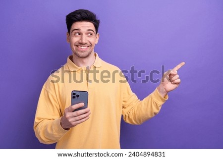 Photo of charming cute man dressed yellow shirt texting apple iphone samsung device showing empty space isolated purple color background