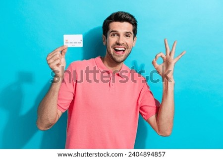 Portrait of young funny person guy in pink t shirt shows okey sign recommend debit card advantages isolated on aquamarine color background