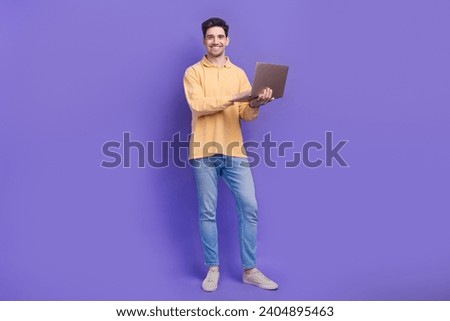 Full length photo of handsome young guy hold netbook work remotely dressed stylish yellow garment isolated on purple color background