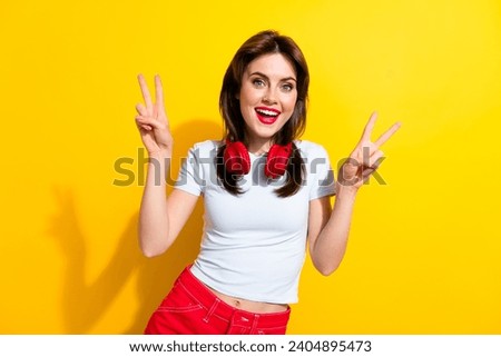 Portrait of good mood pretty girl wear white t-shirt in headphones two arms showing v-sign symbol isolated on yellow color background