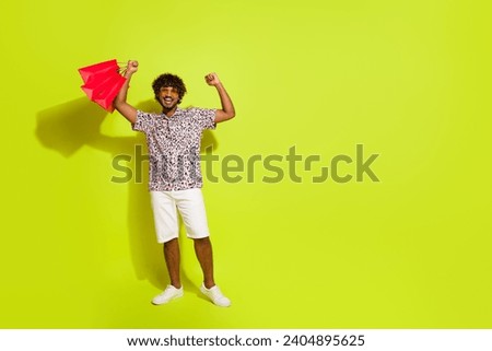 Full size photo of attractive young guy raise fists hold bags dressed stylish pink leopard print outfit isolated on yellow color background