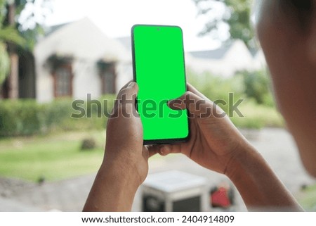 A man's hand is holding a smartphone with a green screen with a garden background in a cafe              