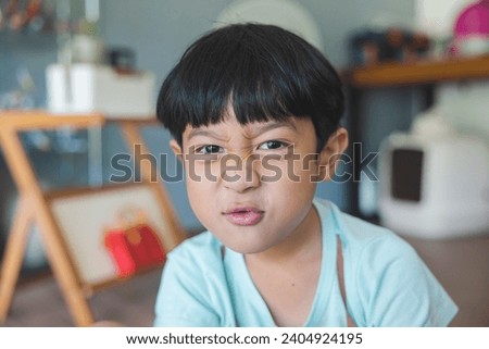 Close up portrait of Asian boy with black bangs, black eyes with a smiling face wearing a light green shirt look at camera and sitting on the floor of his house and hand holding pencil to draw.