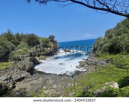 This is a beautiful beach with blue water and surrounding rocks and grass.