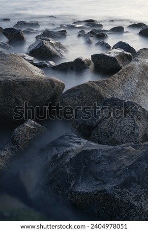A slow shutter speed was used to see the movement and long exposure of misty sea and rocks. Image of breakwater stones in the sea made with a long exposure. High quality photo