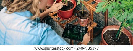 Unrecognizable young woman using digital tablet while caring plants of her urban garden on terrace of residential apartment