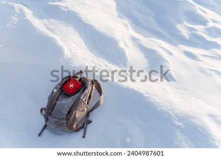 A first-aid kit is on the backpack in the snow in winter, a small red first aid kit, a box with medicines, winter trekking in the mountains. High quality photo