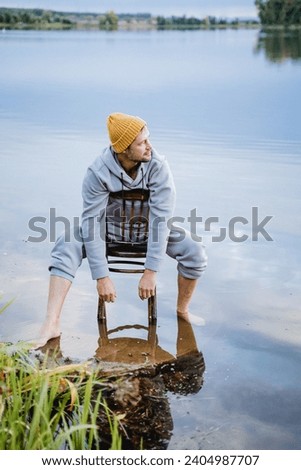 A hipster is resting on a lake, a guy is sitting on a chair in the water, cold water is dipping a man's feet. High quality photo