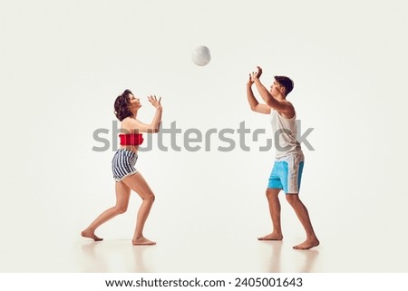 Young people, man and woman, friends playing beach volleyball, having fun on seaside resort against white background. Concept of summer vacation, travelling, retro style, fashion, leisure