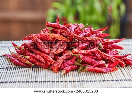 Close up picture on the pile of sun dried red hot chilli peppers on the bamboo or wooden mat in the hot sunny evening after harvest. Dried peppers will be used in the kitchen as a hot spicy condiment.