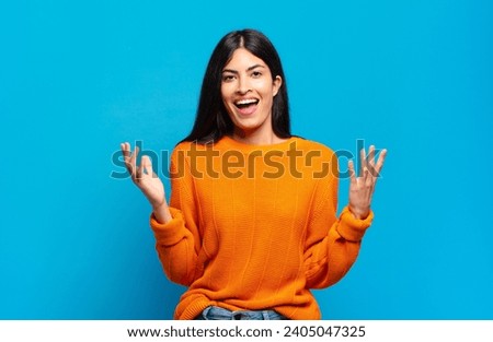 young pretty hispanic woman feeling happy, excited, surprised or shocked, smiling and astonished at something unbelievable