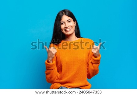young pretty hispanic woman smiling joyfully and looking happy, feeling carefree and positive with both thumbs up