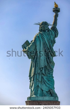 Rear vertical photo of the Statue of Liberty holding her torch on a sunny day in Manhattan, known as the lady of New York City USA.