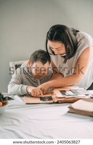 Asian girl points a smiling elderly woman with Down syndrome to a photo in an old album.