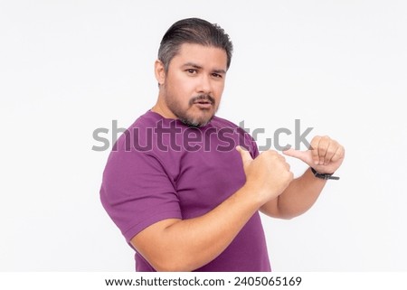 A cocky man points to himself with his thumbs, bragging while looking smug - but looking funny. Wearing a purple waffle shirt. Half body photo isolated on white background. Royalty-Free Stock Photo #2405065169