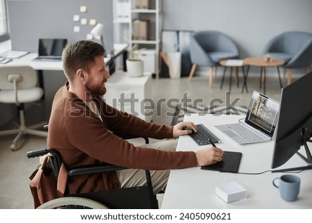 Side view portrait of man with disability editing photos or video at office workplace and using pen tablet, copy space
