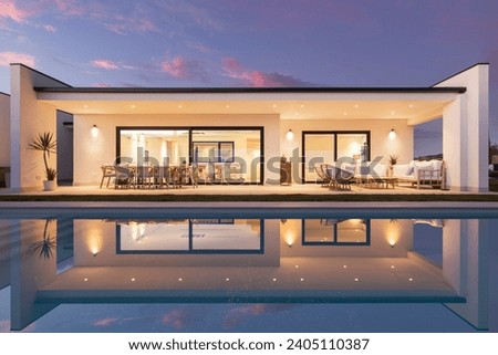 Beautiful façade at sunset of a single-family house with large windows that overlook the living room and kitchen with an exterior porch and the reflection of the house over the pool. Royalty-Free Stock Photo #2405110387