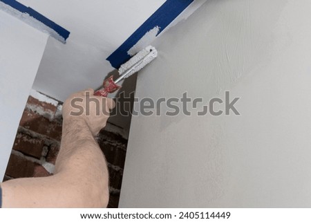 A skilled artisan, using a roller, transforms a large room with precise and masterful painting. Royalty-Free Stock Photo #2405114449