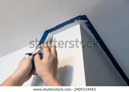 Meticulous hands remove paint tape, unveiling perfectly coated corners for a flawless room finish.
