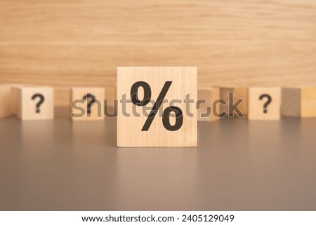 Close-up: A wooden cube with a percentage sign rests on the table, small wooden cubes with question marks in the background. Concept: Financial Puzzle. 