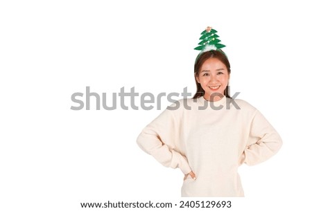 Confident young asian woman putting both hands on her hips while smiling and wearing a Christmas tree headband against a white background