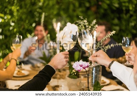 A dinner table full of guests celebrates by toasting their wine glasses together in a cheers. 