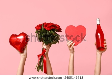 Female hands holding roses, bottle of wine, heart-shaped balloon and gift box on pink background. Valentine's Day celebration Royalty-Free Stock Photo #2405149913