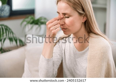 overworked woman with headache touching her nose bridge feeling tired and stress. sick young female with nasal discomfort suffering from sinusitis or respiratory infection Royalty-Free Stock Photo #2405152617