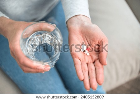 high angle view of female hand hold glass of water and medication pills in palm, taking sedative tablets from anxiety disorder. woman with daily dose of vitamin supplements for healthy life, top view Royalty-Free Stock Photo #2405152809