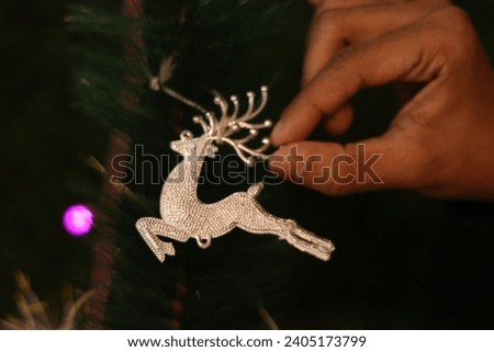 Closeup of hand of An indian boy decorating christmas tree with artificial Silver reindeer, decorating items