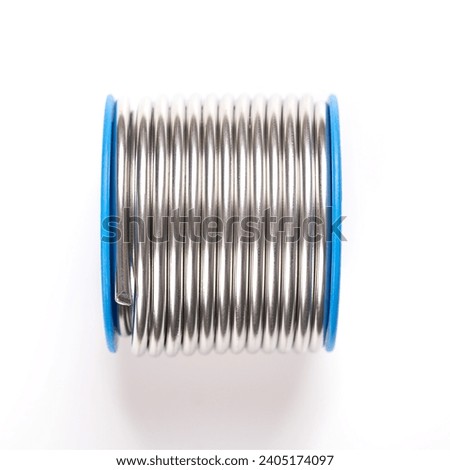 Spool of soft solder wire, with a diameter of 3 millimeters. Fittingslot, fusible metal alloy of tin and copper, used to create a permanent bond between metal workpieces. Close-up, from above. Photo. Royalty-Free Stock Photo #2405174097
