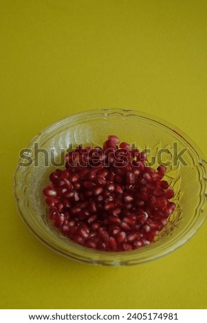 a cup of pomegranate seeds with yellow background