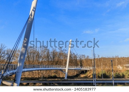 Cable-stayed bridge for bicycles and pedestrians over highway towards Hoge Kempen national park, bare trees against blue sky in background sunny autumn day in As Limburg, Belgium Royalty-Free Stock Photo #2405183977
