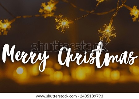 Merry Christmas text on stylish glowing snowflake christmas garland on background of golden lights bokeh in evening. Happy Holidays! Season's greeting card. Handwritten sign
