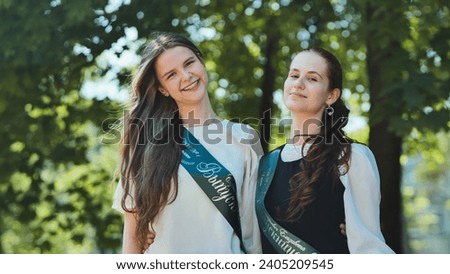 Portrait of two Russian schoolgirls graduating from high school with a ribbon and the name - Graduate 2023 on it.
