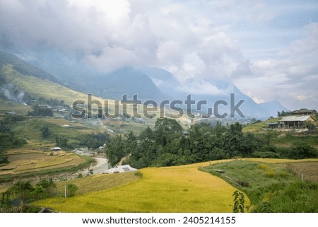 The traditional village on the mountainsides with tropical forests with green and yellow rice terraces, in Asia, Vietnam, Tonkin, Sapa, towards Lao Cai, in summer, on a cloudy day. Royalty-Free Stock Photo #2405214155