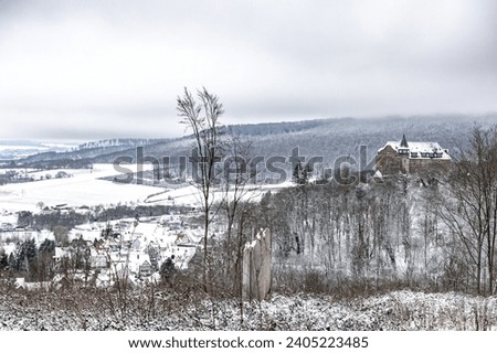 Winter landscape with a gloomy sky and an ancient castle on a hill in the middle of a forest, snowy fields around