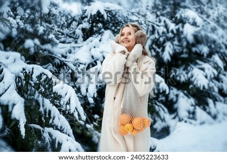 Portrait of a beautiful girl with oranges in a bag. A girl stands in a winter forest against a background of snow-covered fir trees. Walk through the forest