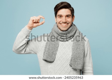 Young ill sick man wear gray sweater scarf hold in hand pill tablet medication isolated on plain blue background studio portrait. Healthy lifestyle disease virus treatment cold season recovery concept Royalty-Free Stock Photo #2405235963