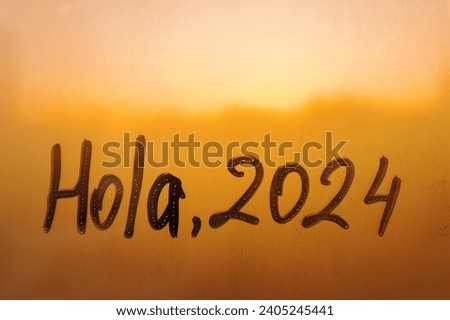 lettering Hola in Spanish is hello in english and numbers 2024 paint with finger with streaks of water on splashed by rain foggy glass on orange window