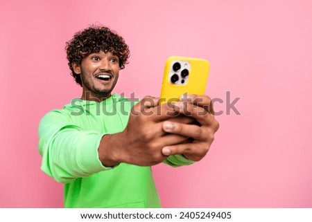 Photo of positive indian guy wear green hoodie laughing holding his smartphone using for promoting blog isolated on pink color background
