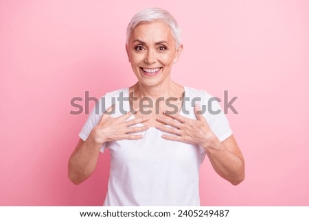 Photo of impressed positive woman with short hairstyle wear white t-shirt holding palms on chest staring isolated on pink background