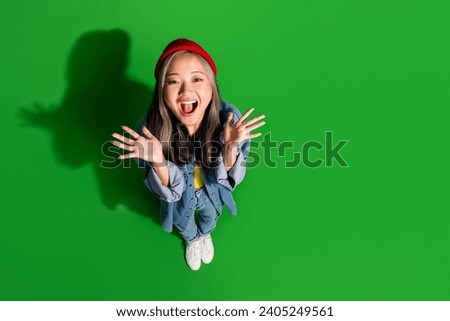 Full length top view photo of pretty impressed girl dressed jeans shirt rising hands arms empty space isolated green color background