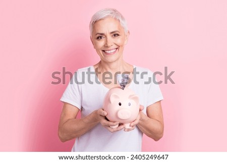 Photo portrait of lovely senior lady hold piggy collect money dressed stylish white garment isolated on pink color background