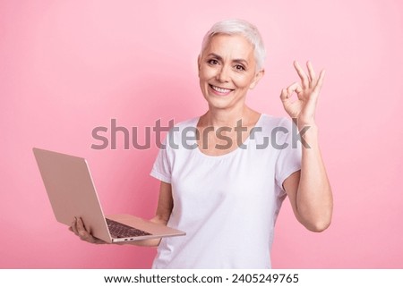 Photo portrait of lovely senior lady show netbook show okey symbol wear trendy white garment isolated on pink color background